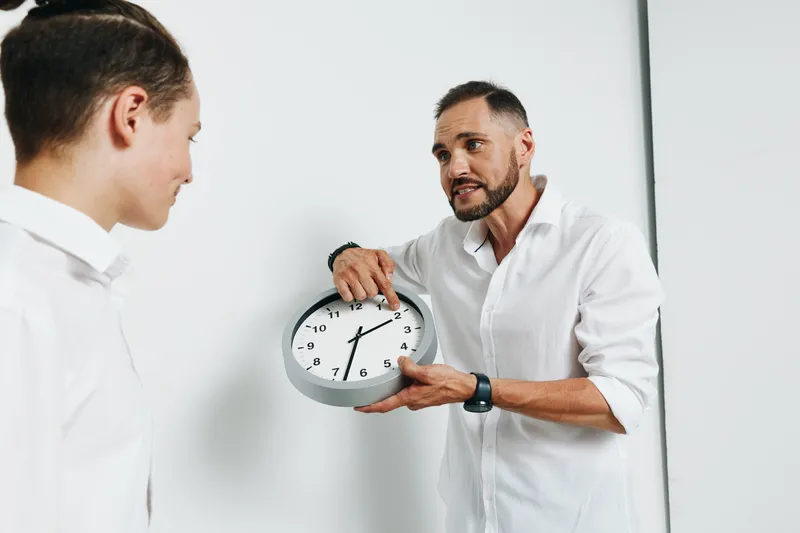 A professional business man explains time management to a colleague, showing focus and urgency against an isolated white background, with a calm, confident demeanor.