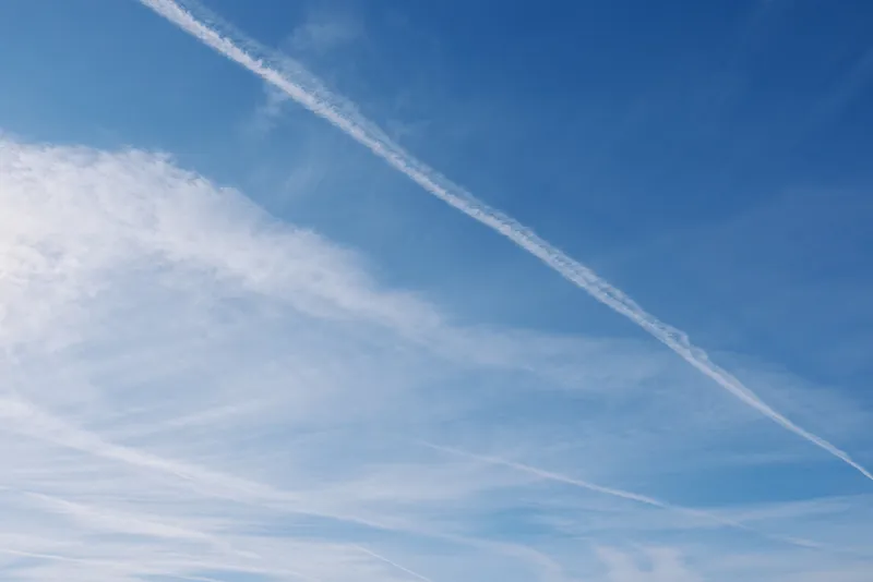 Blue sky with white contrails and wispy clouds, airy trails cross the expanse, tranquil daytime atmosphere with open space and calm horizon above
