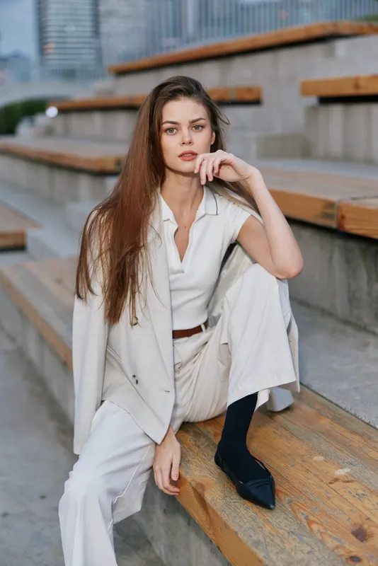 woman fashion portrait with long hair in white outfit sitting on wooden stairs urban outdoor