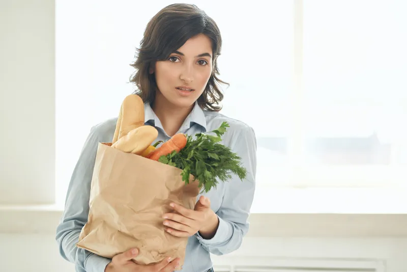 Милая брюнетка держит продуктовую сумку с овощами, пропагандируя здоровое питание и образ жизни