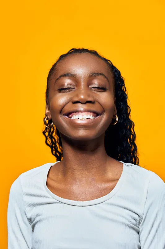 Happy African girl with curly hair smiling brightly against a vibrant yellow background, showcasing joy and positivity