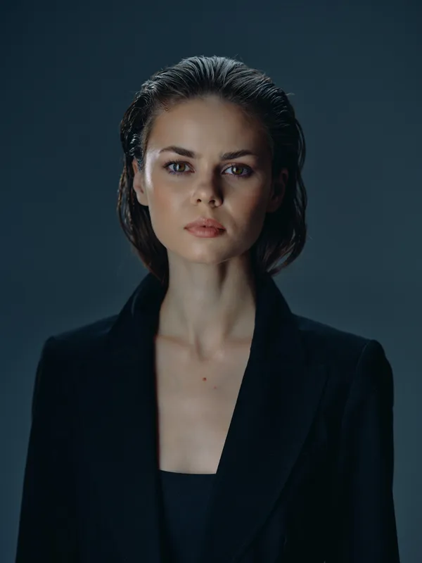 Serious woman portrait with wet hair wearing black blazer in dark studio setting, minimalist and moody atmosphere