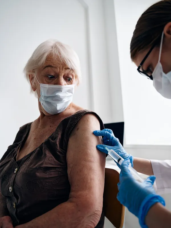 Врач делает пациенту инъекцию вакцины от COVID-19 и оформляет вакцинный паспорт