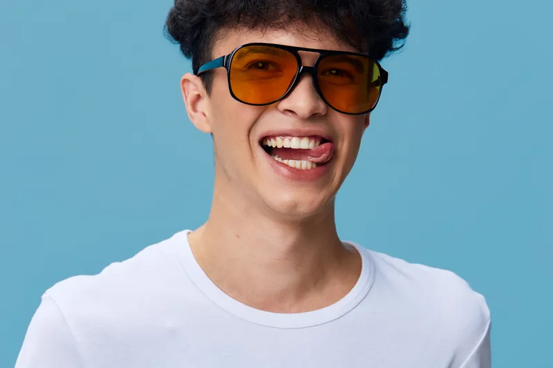 smiling man wearing yellow sunglasses and white t-shirt showing playful expression against blue background, casual style, youthful energy