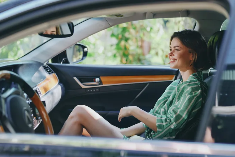 A relaxed woman sits in a stylish car interior, smiling as natural light filters through the cabin and dashboard.