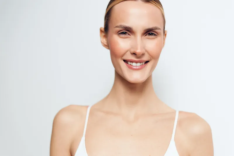 Woman with a smile, skincare closeup on face and neck, beauty portrait, soft studio lighting on clean white background, wellness and selfcare concept, calm happy mood
