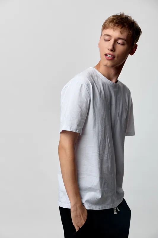 Young man wearing a white t shirt poses in a clean studio, showcasing casual fashion, relaxed attitude, simple background and natural lighting for lifestyle or e commerce use