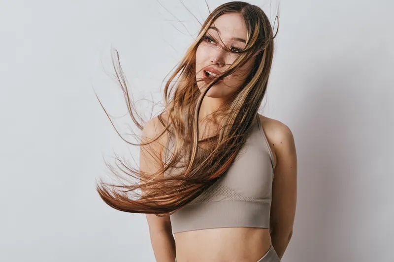 Young woman with long hair in motion wearing beige crop top and leggings against white background. Fitness, beauty and casual style with natural look and soft lighting.
