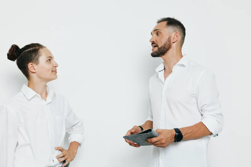 A professional man in a business setting stands against an isolated colored background, engaging in a thoughtful discussion with a colleague. Emotions show confidence, focus, and engagement as ideas