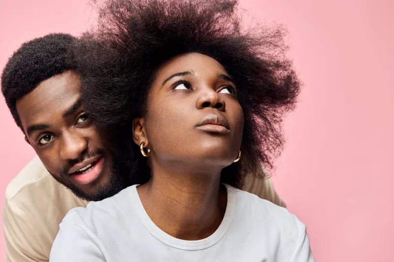 Happy couple with natural hair posing on a pink background, showcasing love and connection through expressive emotions and stylish casual wear