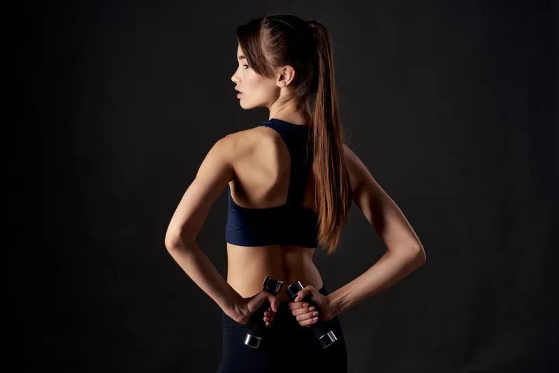 Спортивная женщина с гантелями в руках на тренировке на тёмном фоне