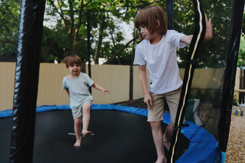 Active boys playing on a trampoline, enjoying a sunny day with laughter and excitement in a vibrant outdoor setting surrounded by trees.