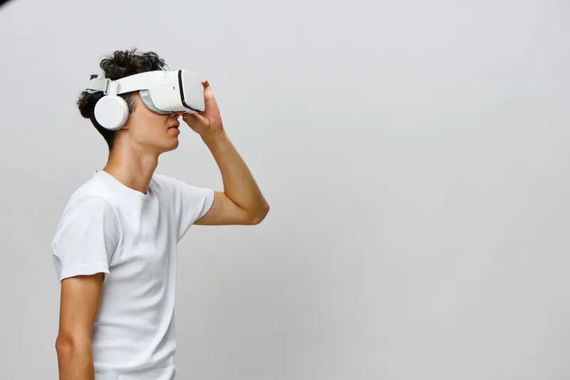 Молодой человек погружен в опыт виртуальной реальности, на нем белая VR-гарнитура и наушники