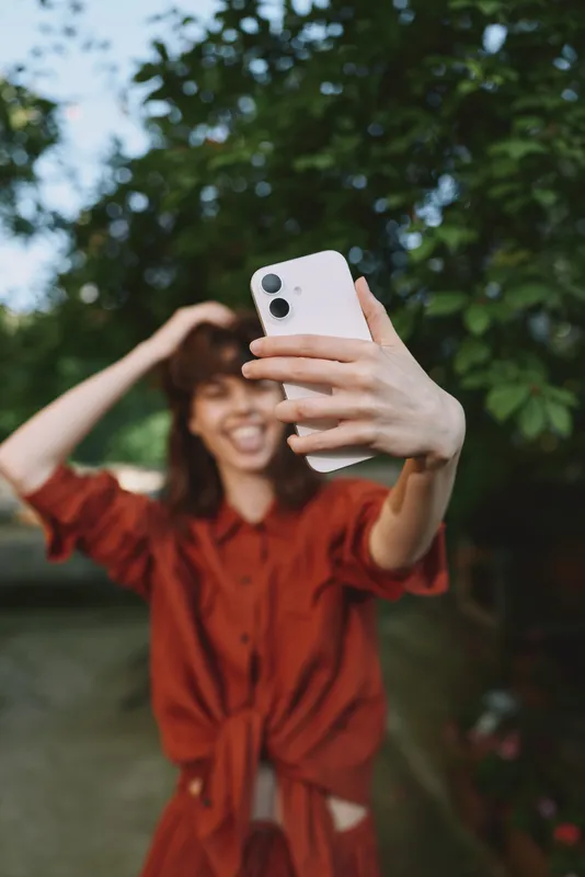 Vibrant woman lifestyle outdoors selfie moment, smiling in a red dress with greenery and sunlight, candid and natural, energetic and cheerful, relaxed pose, warm breeze, vivid colors, joyful