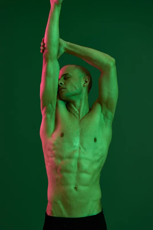 Athletic man posing gracefully under dramatic green lighting, showcasing strength and artistry in this dynamic capture. Emphasizing the beauty of form and movement.