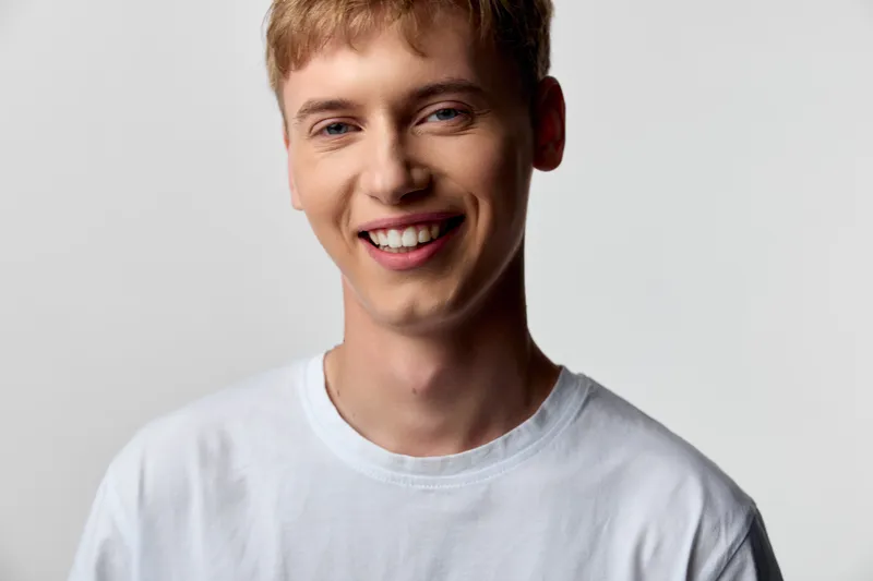Smiling man in a casual studio headshot wearing a white shirt, conveying friendliness and approachability for lifestyle, fashion or corporate use. Bright lighting highlights a clean, modern vibe and
