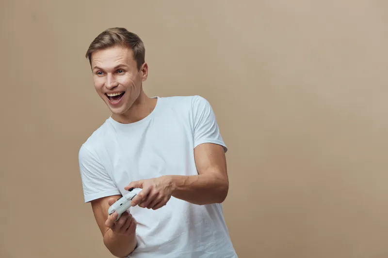 excited young man wearing white t-shirt hold game controller play video games isolated on beige background digital entertainment concept
