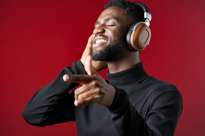 Happy young Black man enjoying music with headphones on a vibrant red background, expressing joy and relaxation through music appreciation
