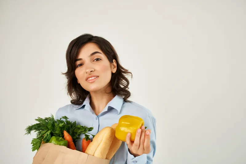 Женщина в голубой рубашке держит пакет с продуктами здорового питания на светлом фоне