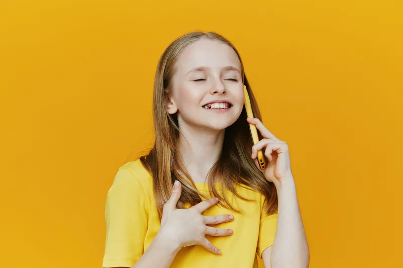 Smiling girl talking on phone, wearing a yellow shirt against a yellow background, expressing happiness and joy in a vibrant and cheerful atmosphere