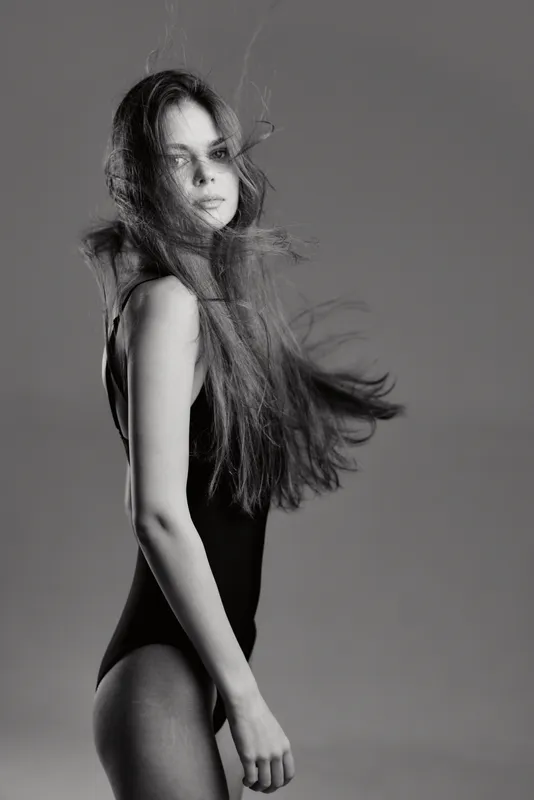 black and white portrait of a young woman with flowing hair wearing a black bodysuit in motion