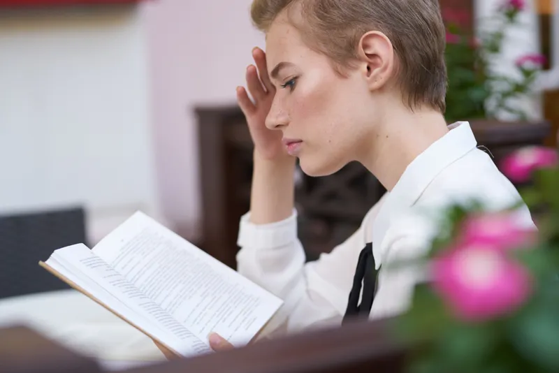 Студент с книгой в руках отдыхает на свежем воздухе, весело прогуливаясь по городу