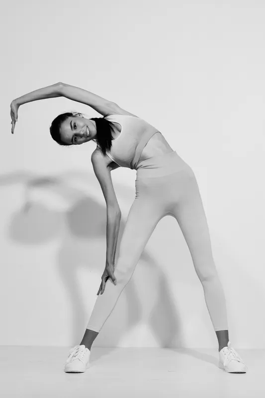 woman sport fitness stretching in monochrome, wearing activewear, indoor exercise, flexible pose, focused expression, minimalist background.