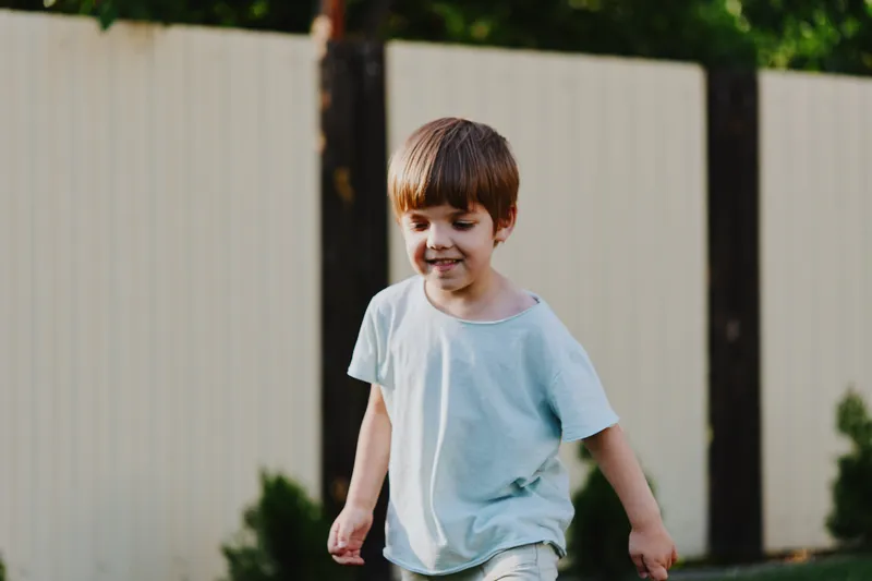 Happy boy playing outdoors, enjoying a sunny day with greenery in the background, showcasing the joy of childhood and carefree moments.