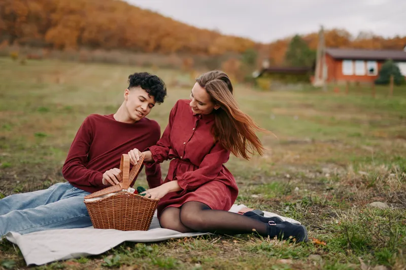 An authentic moment between a couple on a picnic in autumn, showcasing simple joy and natural interaction as they share food and laughter on a grassy field.