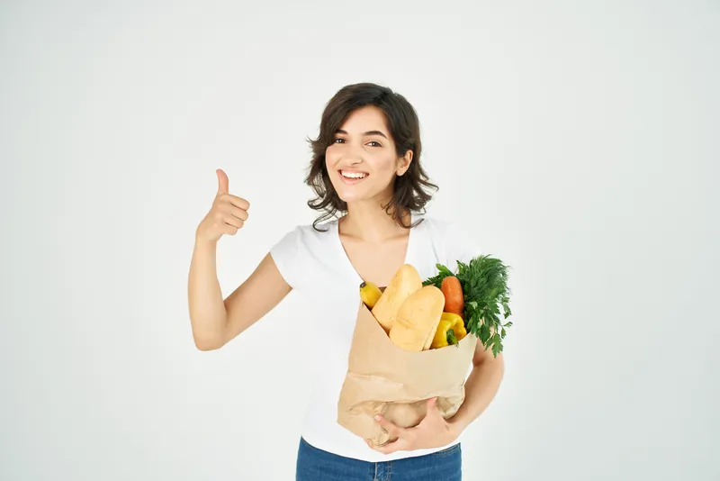 Весёлая женщина позирует с одинаковыми пакетами продуктов в супермаркете
