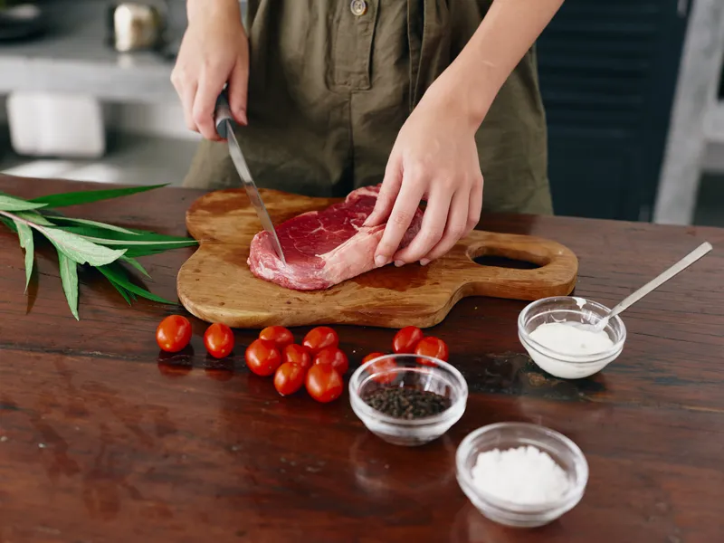 Женщина с ножом в руке нарезает стейк для жарки на кухне