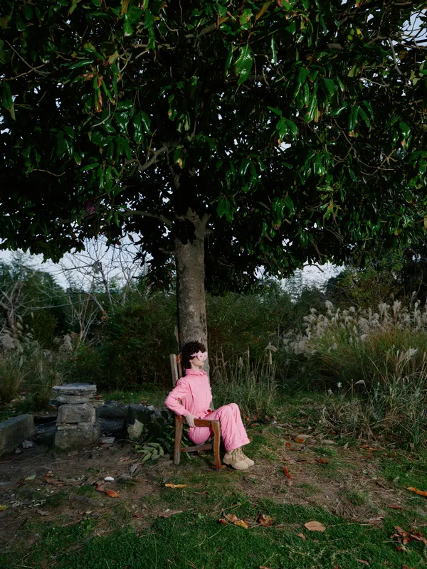 Person garden outdoor tree sitting chair pink dress relaxation nature under shade in a calm countryside scene, showcasing a peaceful moment of leisure in a rustic park