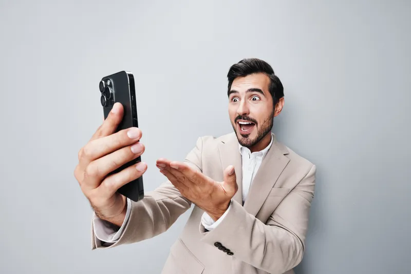 Счастливый мужчина в деловом костюме серого цвета держит смартфон и улыбается