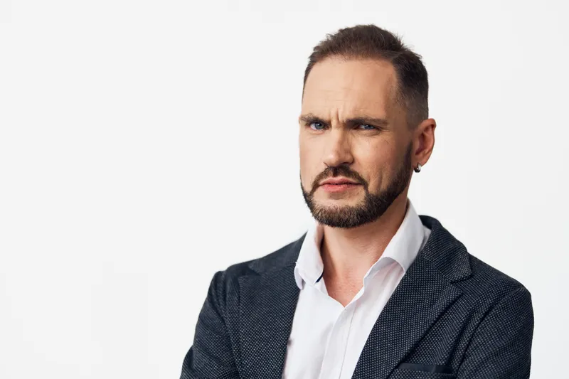 A confident business professional man stands against a solid colored background, conveying a focused mood and strong presence. His expression blends determination with calm, signaling leadership and