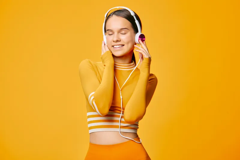 Fitness woman in a sporty orange outfit enjoys music with headphones, dancing and moving against a vibrant orange backdrop, showcasing energy, focus and wellness during a light workout.