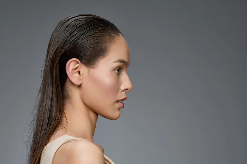 Profile of an elegant woman with wet hair, showcasing natural beauty and confidence against a soft gray background, ideal for beauty and fashion themes