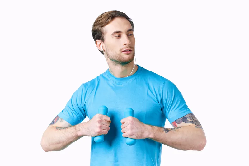 Атлет с гантелями выполняет упражнение, занимается фитнесом, накачанные мышцы рук, татуировка