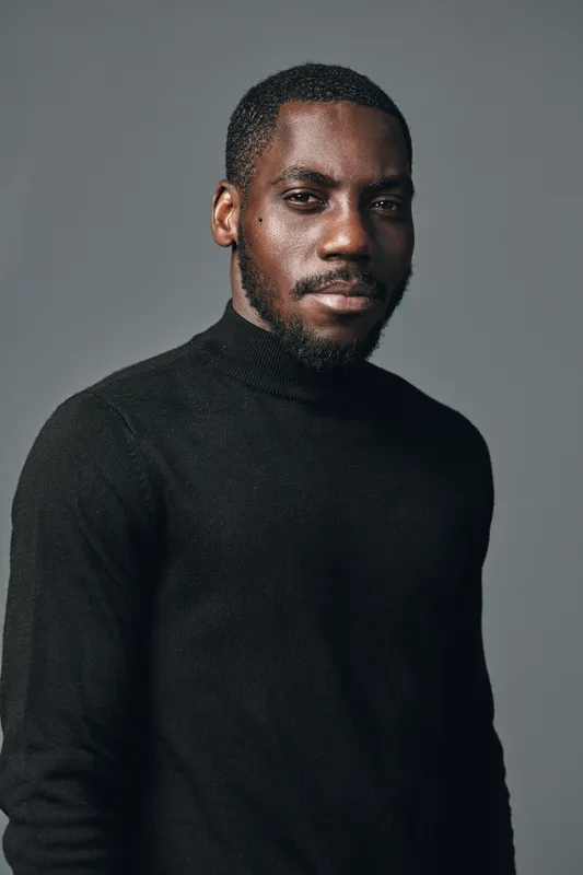 African man portrait in creative conceptual visual style wearing black turtleneck sweater with confident expression on gray background studio shot.