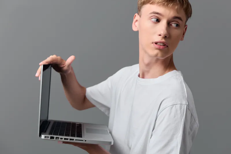 Young man holding a laptop, looking to the side, casual white tee, modern tech concept, portable computing, creative moment, contemporary work vibe