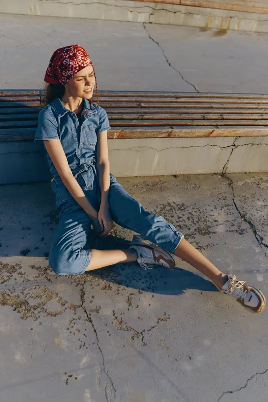 Lifestyle woman in modern boho-western denim street style wearing a red bandana, relaxing outdoors in warm sunlight with film color tones.