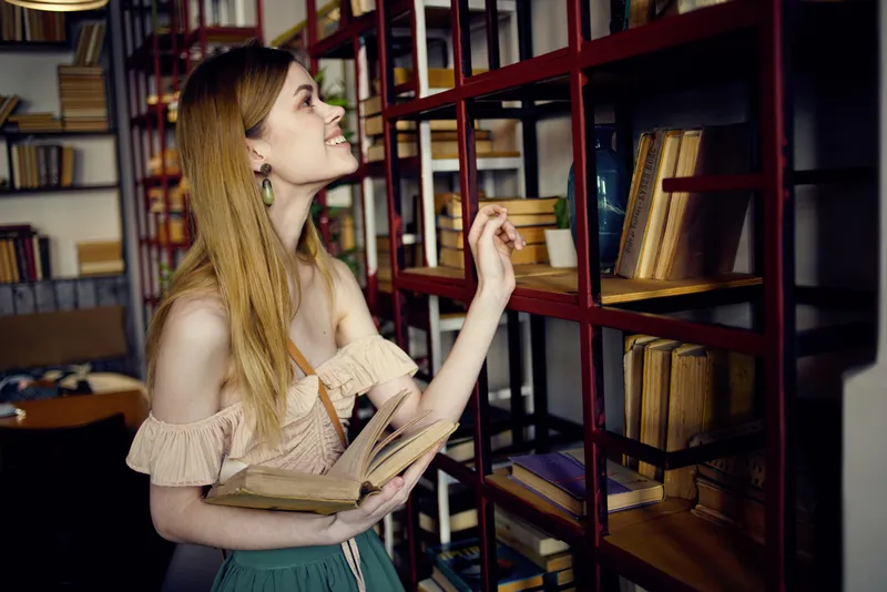 Симпатичная женщина ищет книгу в библиотеке и читает во время отпуска