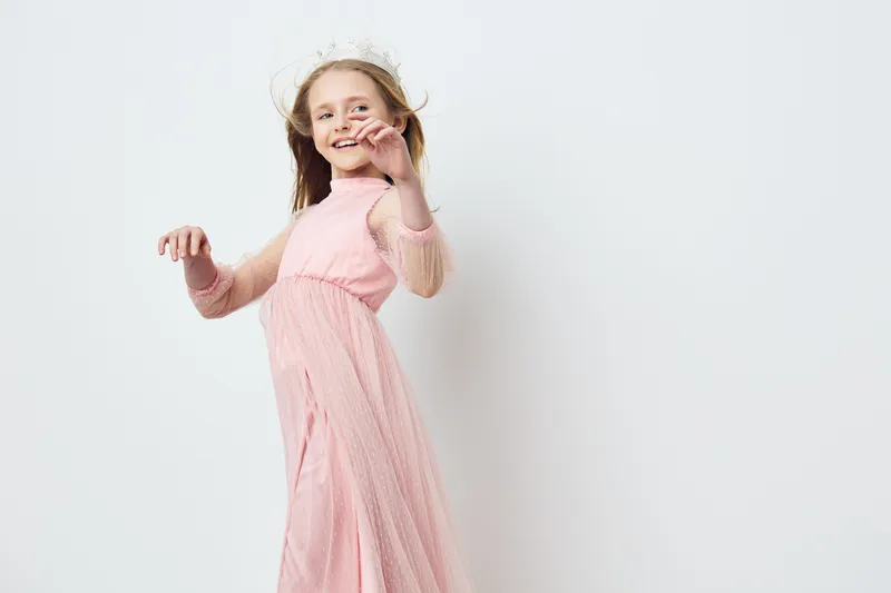 Cheerful young girl in a pink dress playfully dancing against a minimalist background, capturing a sense of joy and innocence in a bright setting