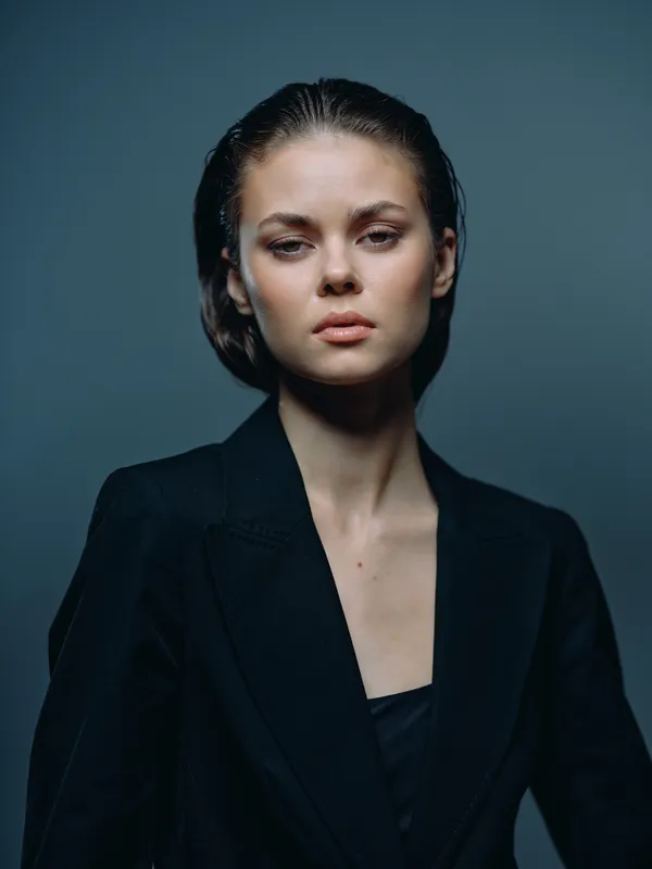 serious woman portrait with dark blazer and low light, studio background, calm expression, fashion style