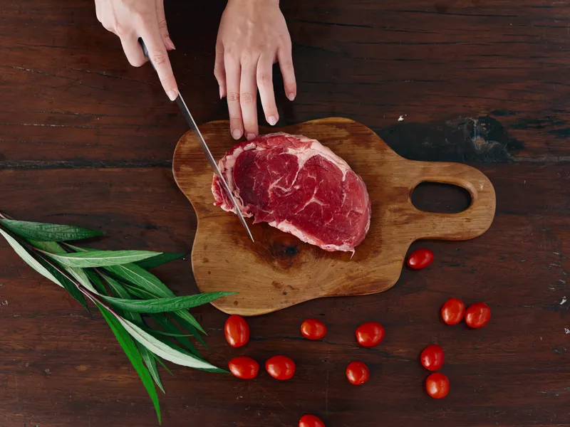 Женщина с ножом в руке нарезает свежее мясо для жарки на кухне