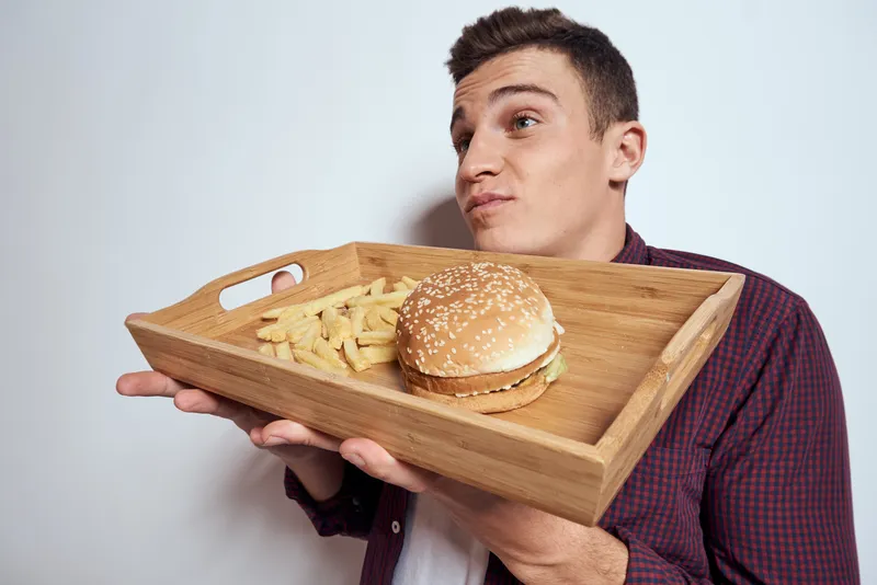 Мужчина ест деревянный поддон, фастфуд, картофель фри, гамбургер, диетическая еда, ресторан, светлый фон
