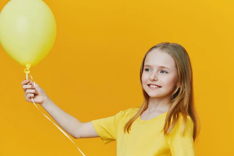 Happy girl holding a yellow balloon against a bright yellow background, wearing a matching yellow T shirt, representing joy and playfulness