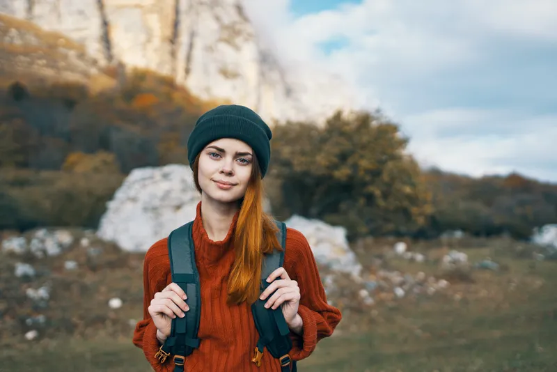 Симпатичная женщина-туристка в кепке на фоне гор и горного пейзажа