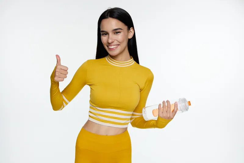 sport fitness woman in yellow activewear holding water bottle smiling and showing thumbs up, healthy lifestyle, energy, hydration, positive attitude