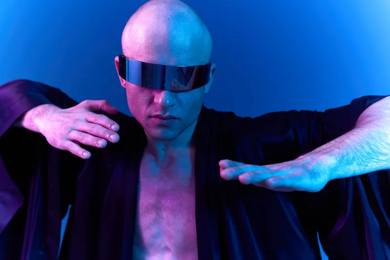 A striking man in futuristic attire showcases a bold pose, exuding confidence and intensity against a dynamic blue background. The scene captures an energetic vibe.