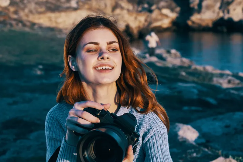 Жизнерадостная женщина-фотограф на открытом воздухе, скалистые горы, профессиональная работа, туризм